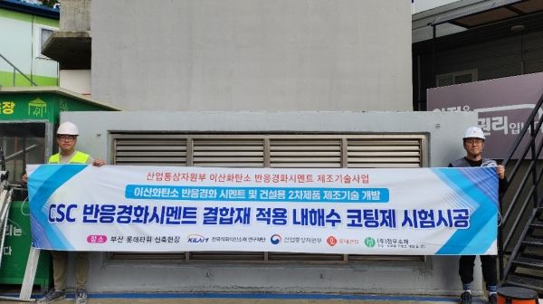 롯데건설 직원들이 부산 롯데타워 현장에서 이산화탄소 반응경화 시멘트를 활용한 코팅제를 시공하고 기념촬영을 하고 있다./사진=롯데건설